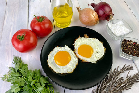 Fried eggs with vegetables, spices and herbs on light wooden background. Traditional European or...