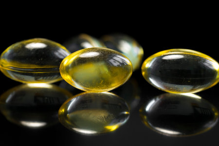 Fish oil capsules isolated on a dark background with reflections, healthy Vitamin supplementation concept, close up shot. Shallow depth of field. Macro.の写真素材