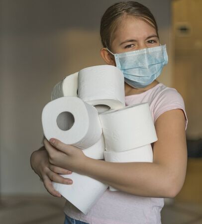 A girl in medical mask holds an armful of toilet paper rolls in her hands. The hype about the demand for toilet paper during the global coronavirus pandemic.の写真素材