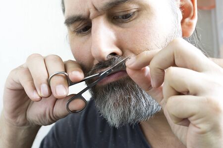 A bearded man carefully cuts his moustache with a small pair of scissors. Close up view.の写真素材