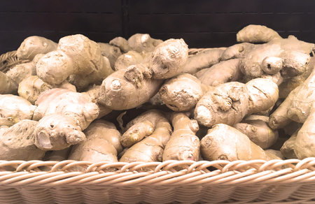 Ginger roots lie in a wicker basket on a black background. Close up view.