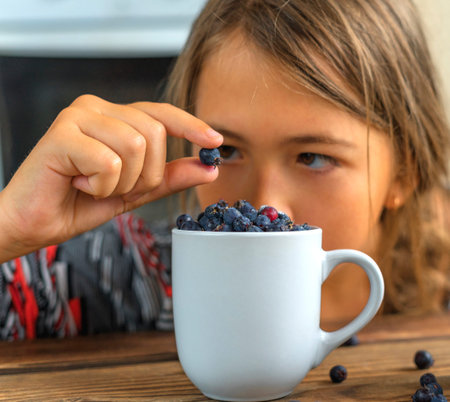 Close-up view of a young caucasian girl with berries. Girl holding one berry in her fingers and...