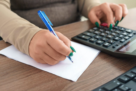 Financial data analyzing. Close-up photo of a businesswomans hand writing and counting on calculator...