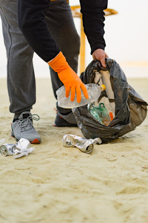 Close-up of male hand in rubber gloves picking up garbage on beach. Environmental ecology pollution concept. Space for text.の写真素材