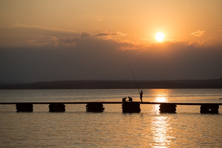 fishermen on a pier watching the sunset meet at the horizonの写真素材