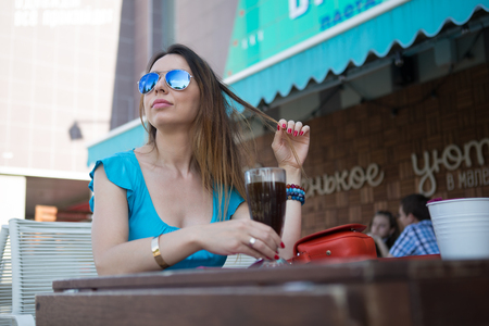 Young woman in a turquoise dress and sunglasses sitting in a barの写真素材