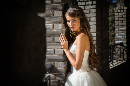 Beautiful innocent brunette bride in white dress posing near church closeupの写真素材
