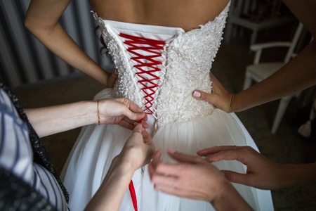 Bride dresses dress in the morning of the wedding day lacing on the back. A closeup image of wedding preparationsの写真素材