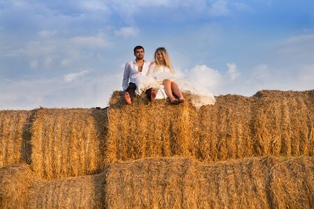 the bride and groom on the background of the sky are sitting on a large haystackの写真素材
