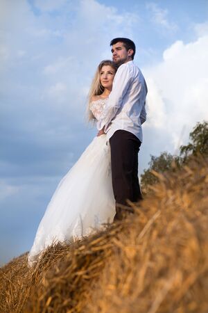 beautiful couple bride and groom standing in the hay against the skyの写真素材