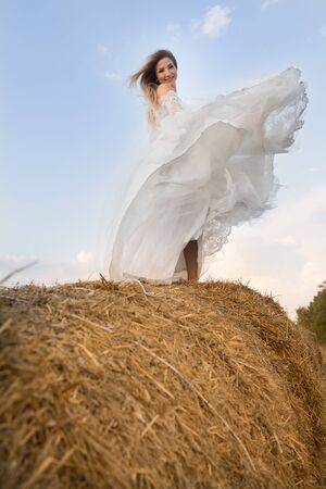 the bride is spinning on a haystack in a white dressの写真素材