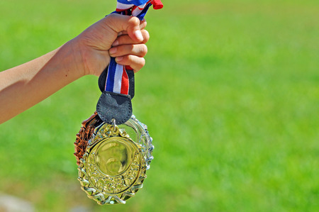 Hand hold gold, silver and bronze medal with green field background.の写真素材
