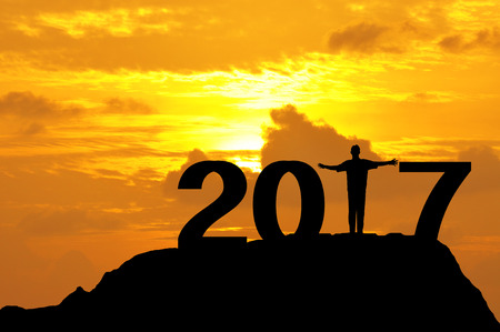 Silhouette of a man open hands on top of mountain during sunset to complete 2017 year.の写真素材