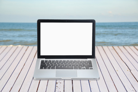 blank screen of laptop on wooden table facing sea with copy space areaの写真素材