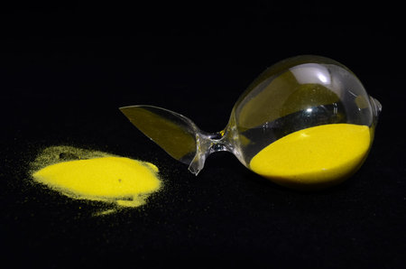 Deadline Concept Broken Hourglass with Yellow Sand on Black Background