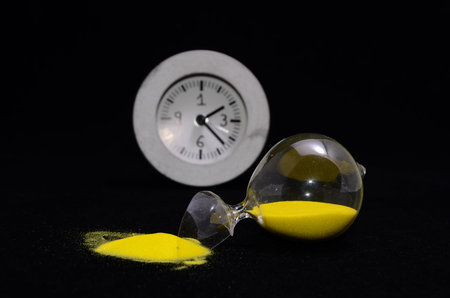 Deadline Concept Broken Hourglass with Yellow Sand on Black Background