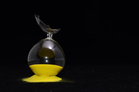 Deadline Concept Broken Hourglass with Yellow Sand on Black Background