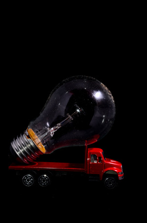 Electric Power Concept Red Truck and Light Bulb on a Black Backgroundの写真素材