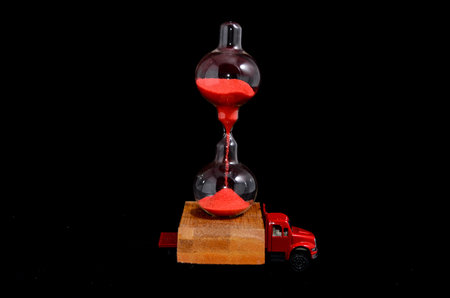 Time Transportation Concept Hourglass Watch on a Red Toy Truck over Black Background