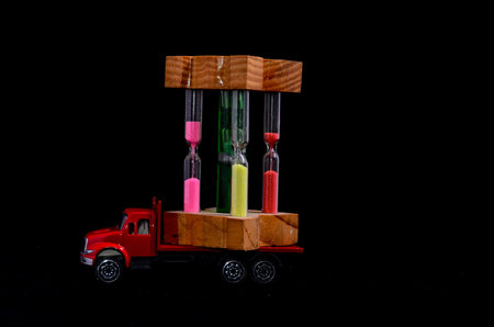 Time Transportation Concept Hourglass Watch on a Red Toy Truck over Black Background