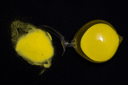 Deadline Concept Broken Hourglass with Yellow Sand on Black Backgroundの写真素材