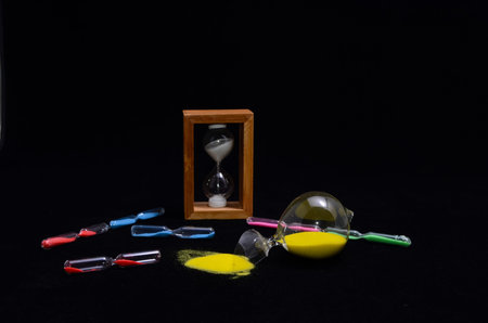 Deadline Concept Broken Hourglass with Yellow Sand on Black Background