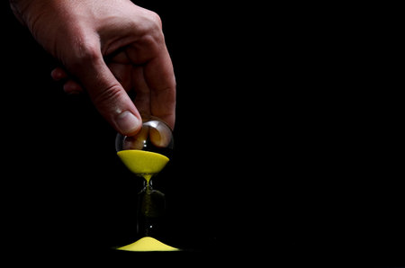 Deadline Concept Broken Hourglass with Yellow Sand on Black Background