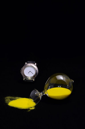 Deadline Concept Broken Hourglass with Yellow Sand on Black Background