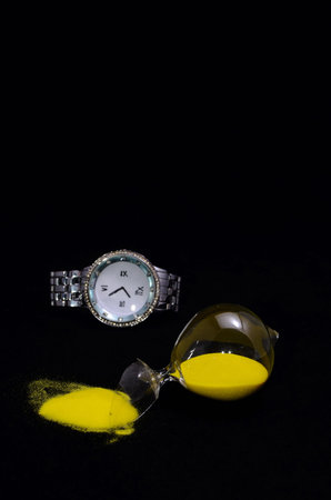 Deadline Concept Broken Hourglass with Yellow Sand on Black Background