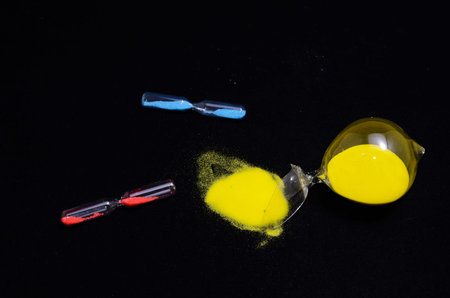 Deadline Concept Broken Hourglass with Yellow Sand on Black Background