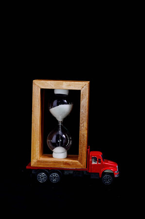 Time Transportation Concept Hourglass Watch on a Red Toy Truck over Black Background