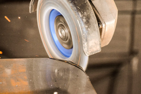 Heavy industry worker cutting steel with angle grinder at car service