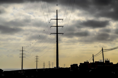 A tall power pole with many wires coming out of it. The sky is cloudy and the sun is settingの写真素材