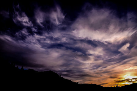 The sky is dark and cloudy with a few clouds in the distance. The sun is setting and the sky is a...