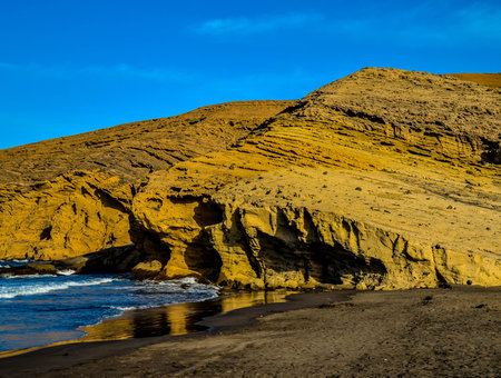 A rocky beach with a cliff in the background. The cliff is covered in rocks and the beach is covered...