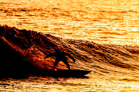 A surfer is riding a wave in the ocean. The water is orange and the sky is pink