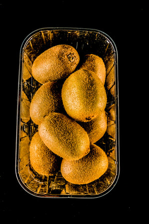A tray of kiwi fruit is displayed on a black background. The kiwi are arranged in a way that they are all facing the same directionの写真素材