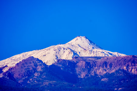 A mountain covered in snow with a blue sky in the background. The mountain is very tall and the snow is very whiteの写真素材