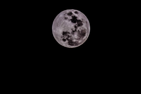 A large, full moon is shining brightly in the night sky. The moon is surrounded by a dark background, emphasizing its size and brightness. Concept of wonder and aweの写真素材