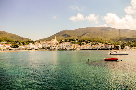 A small red boat sits in the middle of a large body of water. The water is calm and clear, and the...