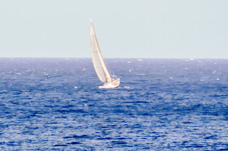 A sailboat is sailing in the ocean. The sky is clear and the water is calm. The sailboat is the only object in the imageの写真素材