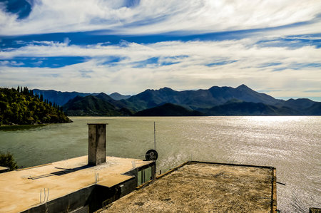 A beautiful view of a lake with mountains in the background. The sky is clear and blue with a few clouds. The sun is shining on the water, creating a sparkling effect. The scene is peaceful and sereneの写真素材