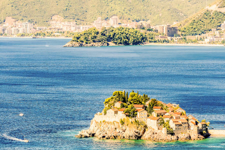 A small island with a few buildings on it is surrounded by water. The water is calm and blueの写真素材