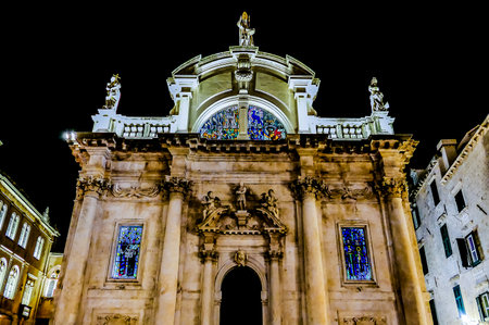 A large building with a stained glass window and a cross on top. The building is lit up at nightの写真素材