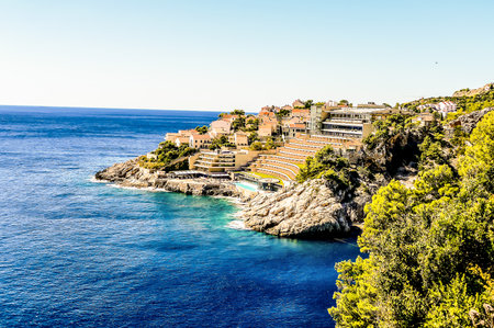 A beautiful blue ocean with a rocky shoreline and a small town in the distance. The water is calm and the sky is clearの写真素材