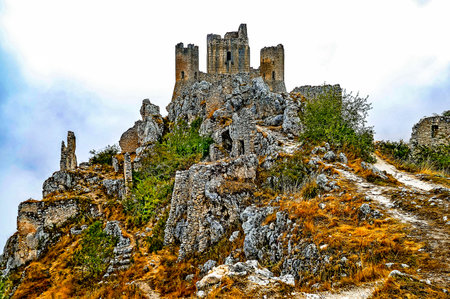 A rocky hill with a castle on top. The castle is old and has a lot of moss growing on it. The hill is covered in rocks and the sky is cloudyの写真素材