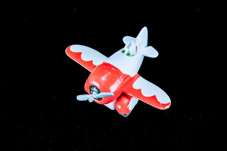 A small red and white toy airplane is flying in the sky. The image has a playful and whimsical mood, as the toy airplane is not a real one but rather a miniature modelの写真素材