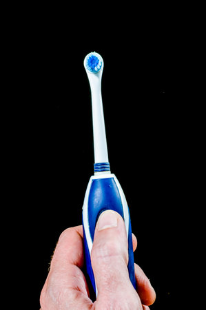 A person is holding a toothbrush with blue bristles. The toothbrush is in a black backgroundの写真素材