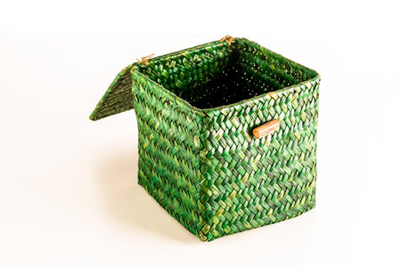 A green woven basket with a brown handle sits on a white background. The basket is open and emptyの写真素材