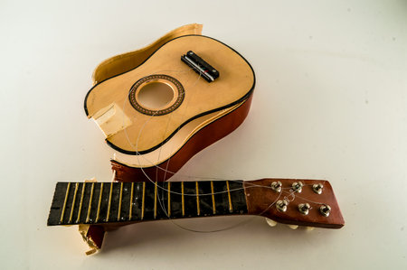A small, toy guitar has been broken, with its neck and head missing. A guitar pick is lying on the ground next to it. The broken guitar appears to be a child's toyの写真素材